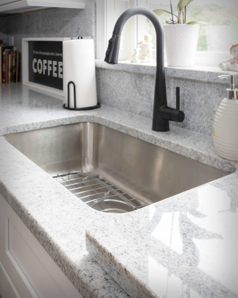 Detail view of sink, matching granite backsplash, and custom granite cutting board near sink in new kitchen and bathroom project in Middletown.