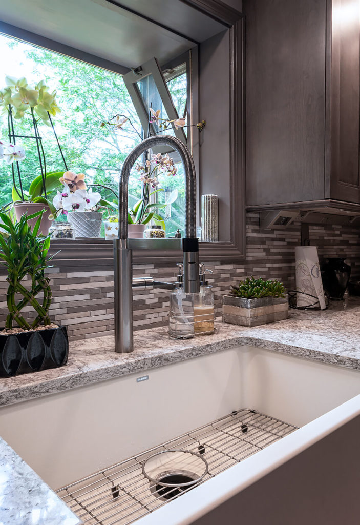 View of the farmhouse sink with apron front, custom tile backsplash, and under cabinet power system from LeGrande.